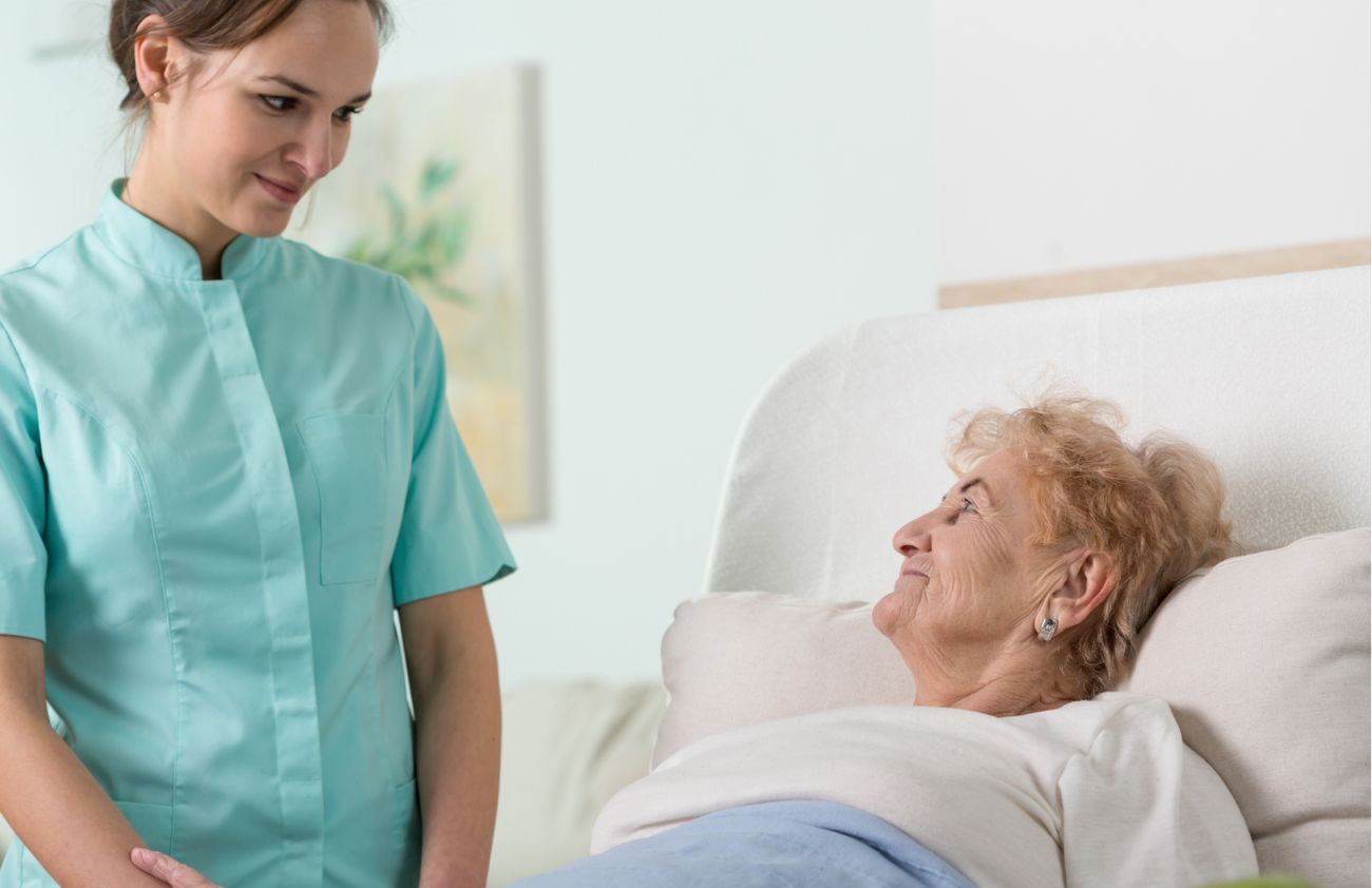 Eine Pflegekraft assistiert einer bettlägerigen älteren Dame, um ihr Wohlbefinden zu fördern.