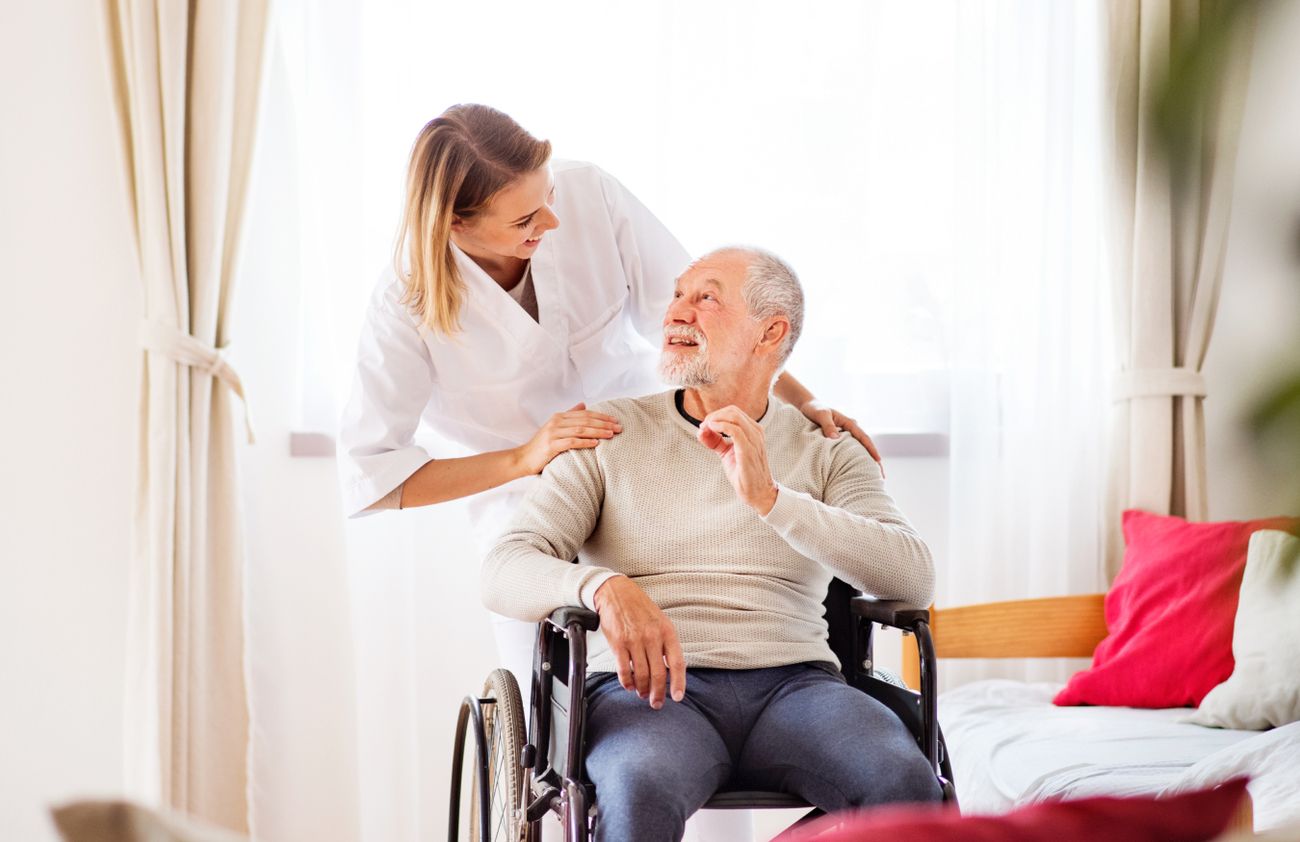 Eine Frau unterstützt einen älteren Mann im Rollstuhl und bietet ihm Hilfe und Begleitung in seiner Mobilität.